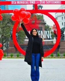 Photo of Laura with a handful of red balloons raised above her head.