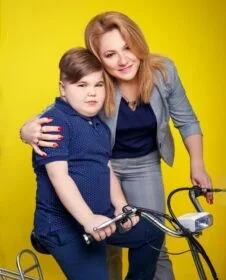 Photo of Maharyta standing next to a child sitting on a bike.