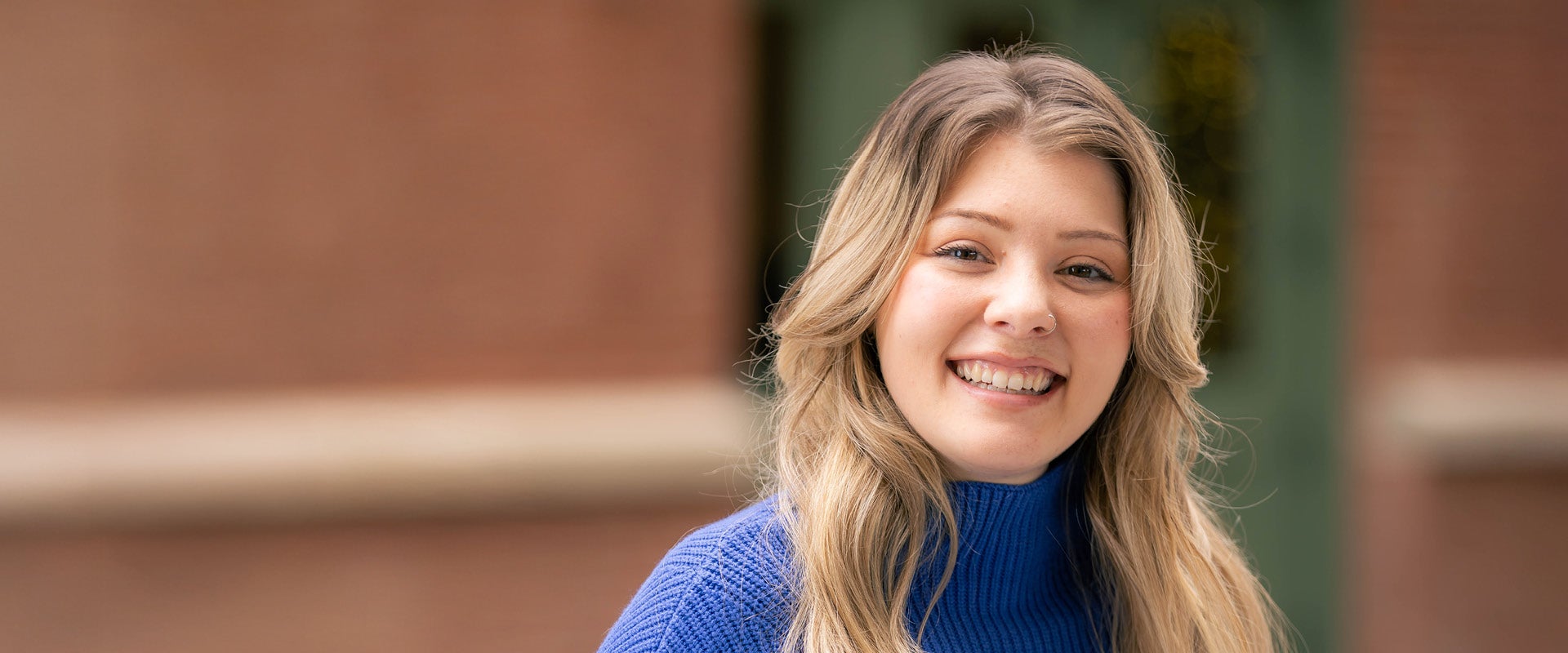Katie, a young woman living with PKU, smiling at the camera and wearing a blue sweater