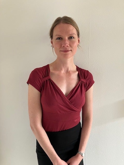 A woman wearing a burgundy shirt standing against a wall background